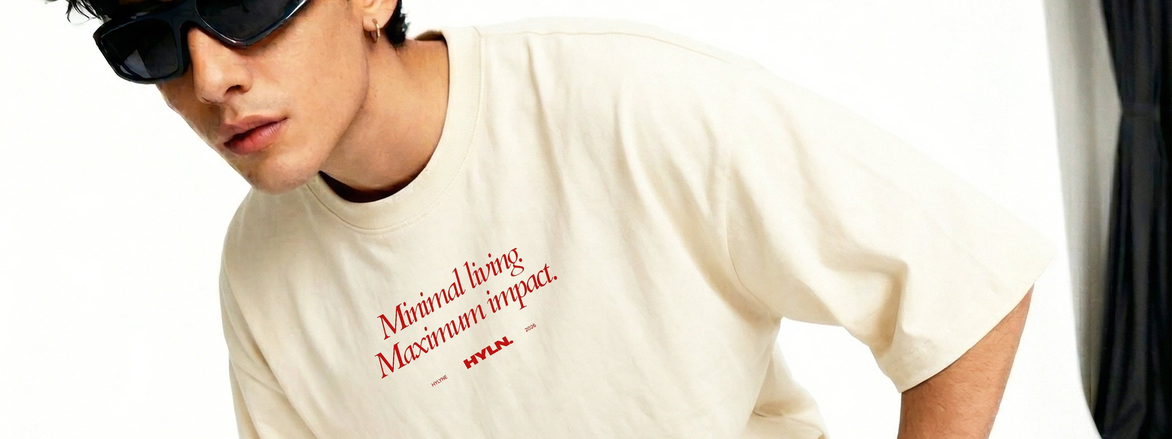 Person wearing a beige t-shirt with text and black pants, posing against a white background.